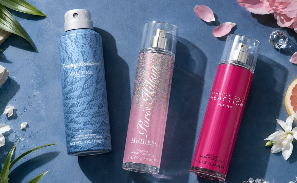 Flat lay fragrance campaign image featuring Tommy Bahama Maritime Journey, Paris Hilton Heiress, and Kenneth Cole Reaction for Her body sprays arranged on a matte blue surface with floral accents, citrus, crystals, and dramatic studio shadows.