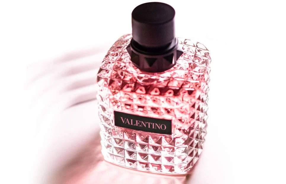 A close-up of a Valentino perfume bottle with a textured glass design and a pink tint, set against a bright white background.