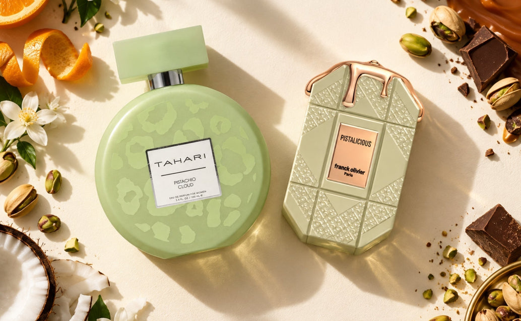 flat lay of pistachio cloud and pistalicious perfume bottles with pistachios, orange, flowers, coconut, chocolate, and caramel on an ivory surface.