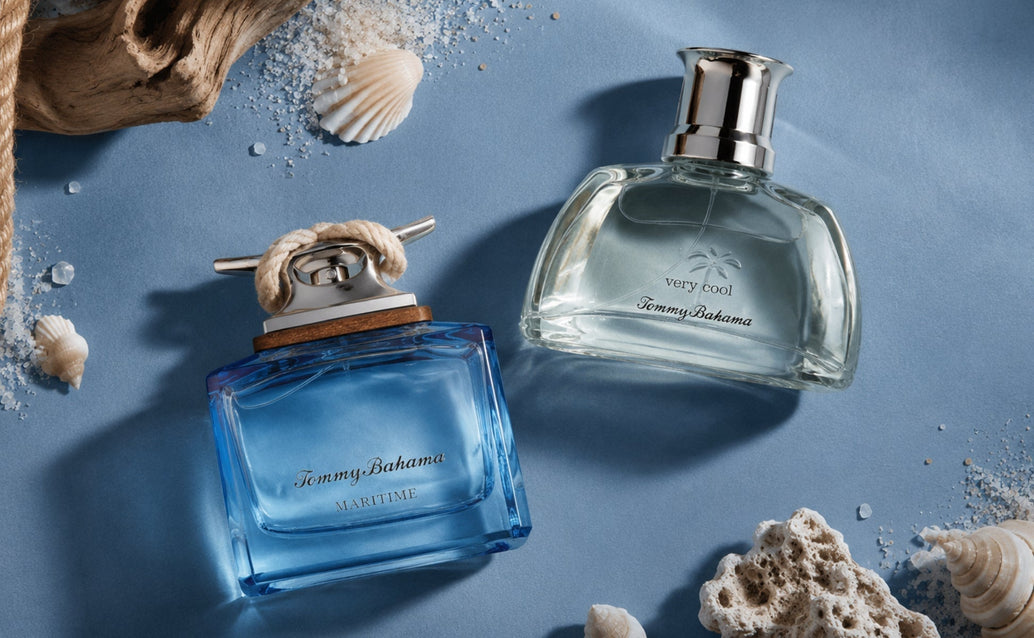 Tommy Bahama Maritime and Very Cool cologne bottles styled in a beach-inspired flat lay on a matte blue surface with shells, rope, and driftwood.