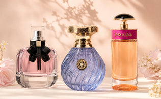 Mon Paris, Milano Mist, and Prada Candy perfume bottles styled on a soft ivory surface with blush florals and warm studio lighting.