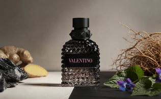 Valentino Uomo Born in Roma bottle with ginger, mineral stones, violet leaves, and vetiver on a matte black surface.