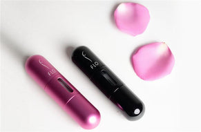 Pink and black FLO perfume atomizers with pink rose petals on a white background.