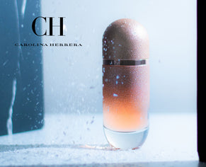 Carolina Herrera perfume bottle with a shimmering gold gradient design, showcased under soft blue lighting with a frosty, winter-inspired background.