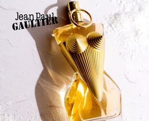 Jean Paul Gaultier perfume bottle in a golden torso-shaped design, displayed on a light surface with soft shadows.