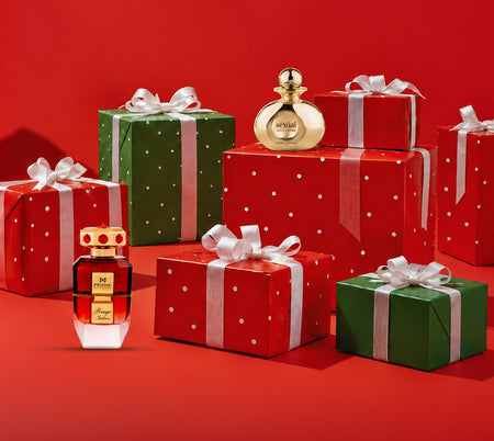 Red and green holiday gift boxes with white ribbons and bows surround two luxury perfume bottles, one gold and one red, against a festive red background.