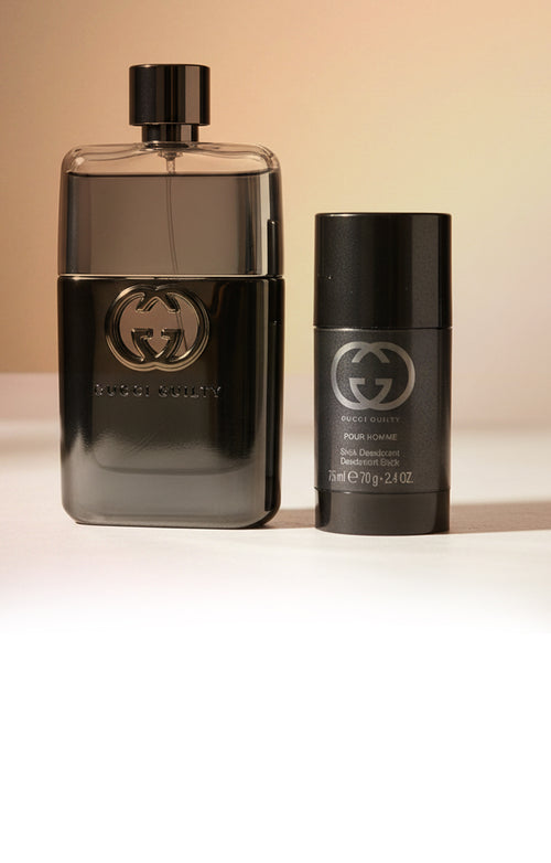 Gucci Guilty cologne and deodorant gift set on a warm beige background.