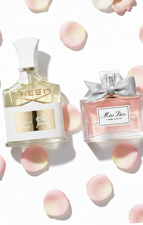 Luxury perfume display featuring Creed Aventus for Her and Miss Dior bottles surrounded by soft pink rose petals on a white background